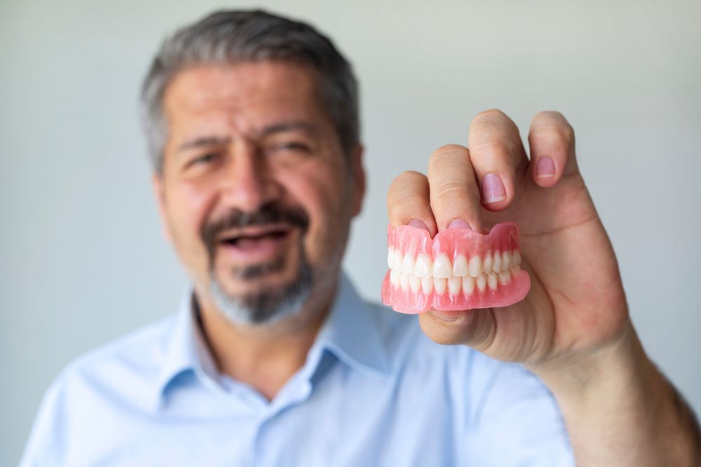 A Man is Holdin  a Denture in His Hand — Dental Prosthetics By Richard & Cindy In Oxenford, QLD