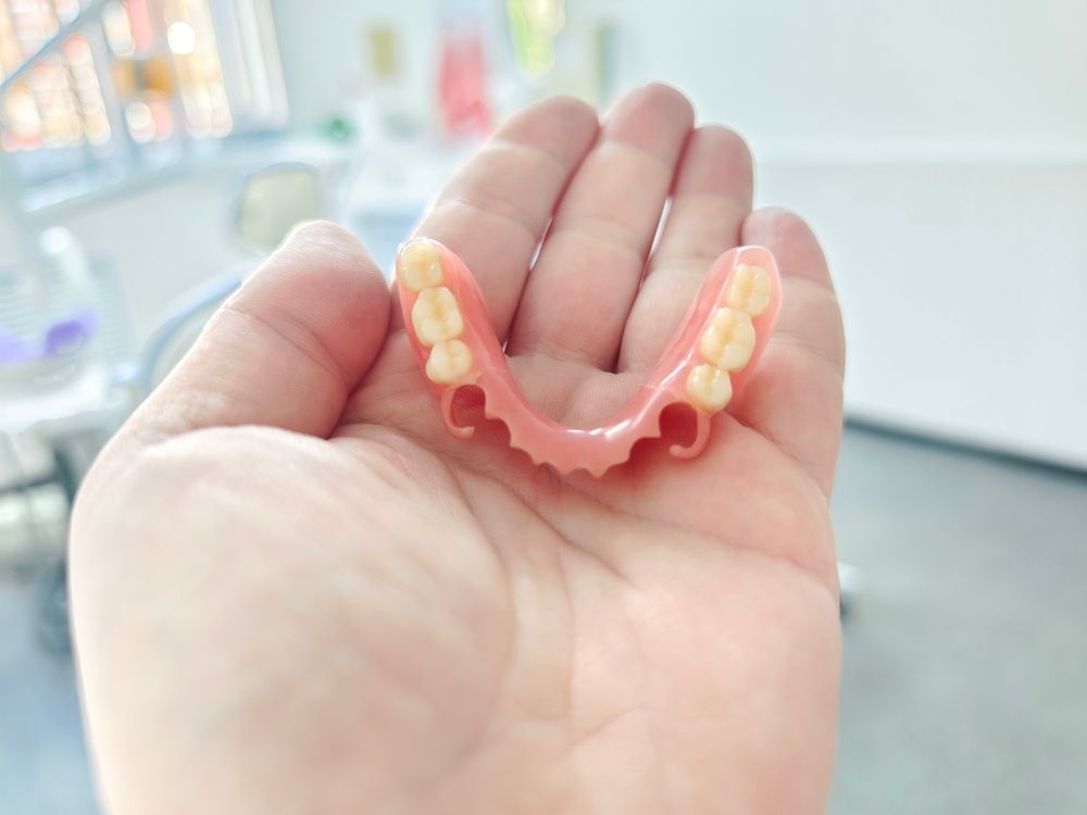 A Person is Holding a Denture in Their Hand — Dental Prosthetics By Richard & Cindy In Oxenford, QLD