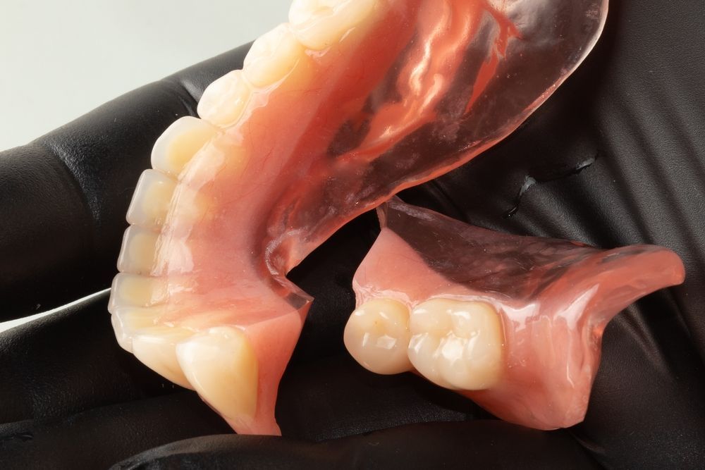 A Person is Holding a Denture in Their Hand — Dental Prosthetics By Richard & Cindy In Oxenford, QLD