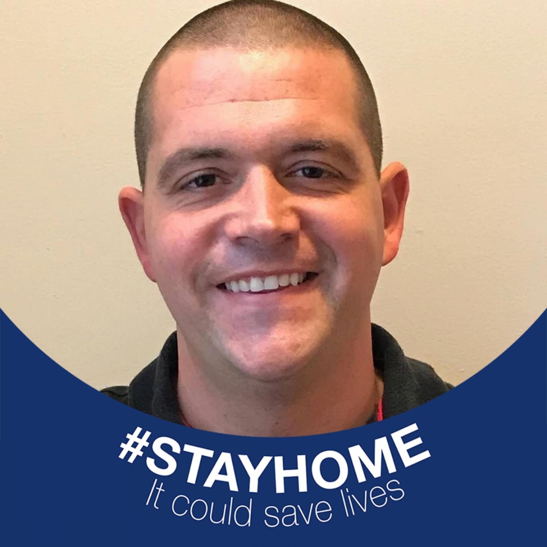 A man is smiling and wearing a #stayhome it could save lives sticker.