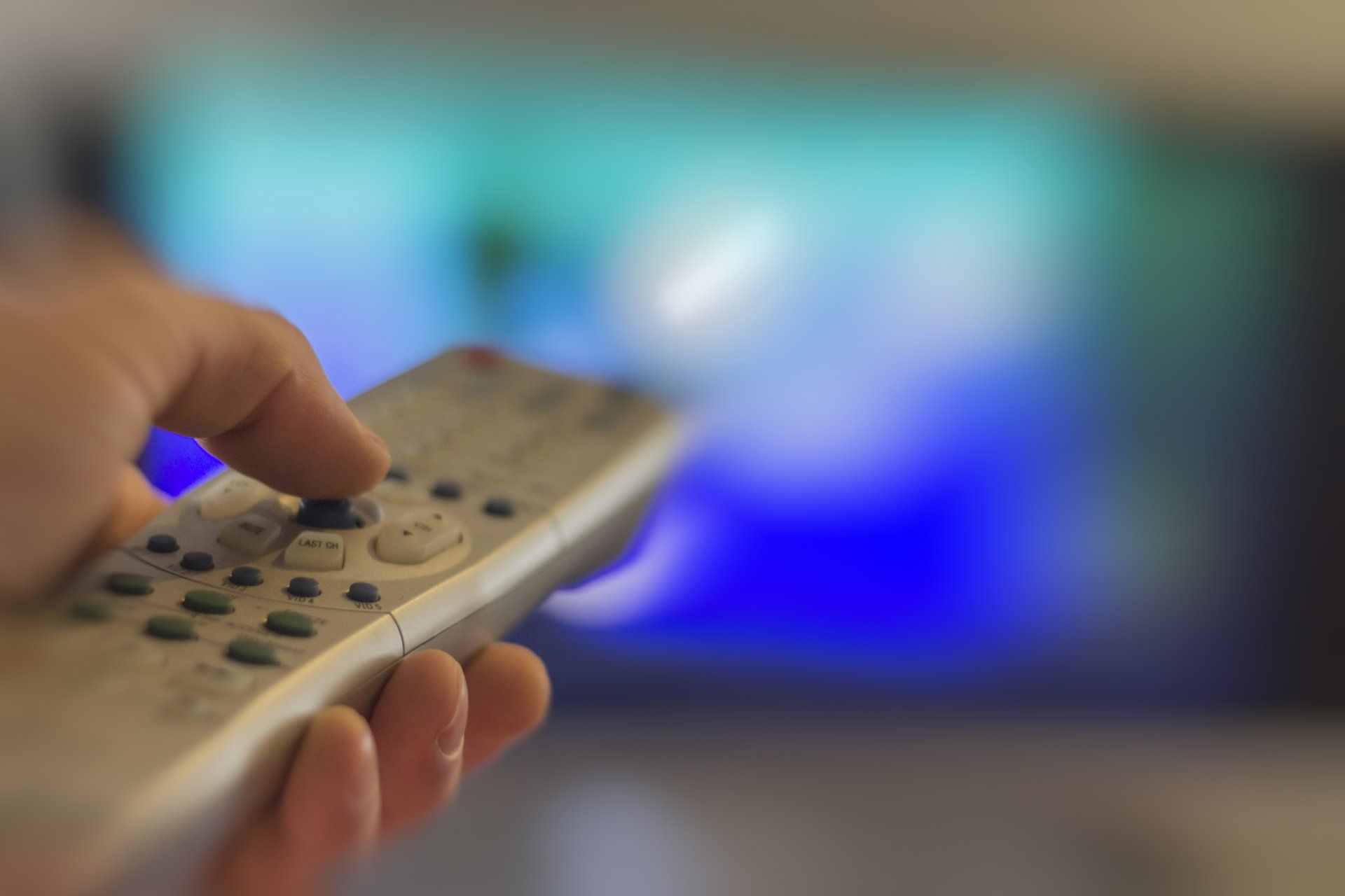 A person is holding a remote control in front of a television.