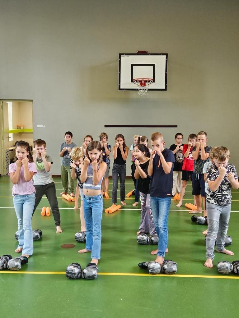 Kinderen in een gymzaal doen boksoefeningen. Ze staan met hun handen omhoog, vlak bij hun gezicht.