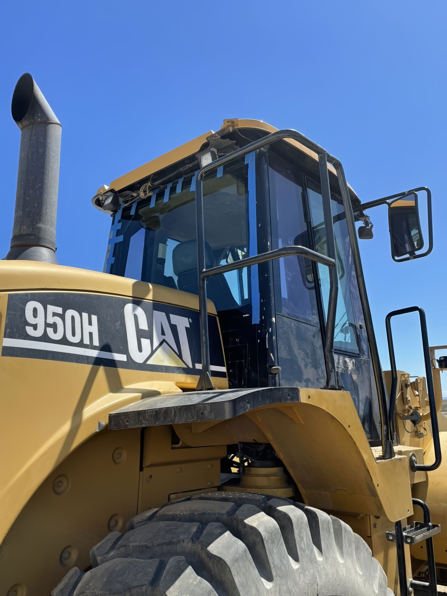 Yellow CAT 950H wheel loader against a blue sky, close-up of cab and front tire