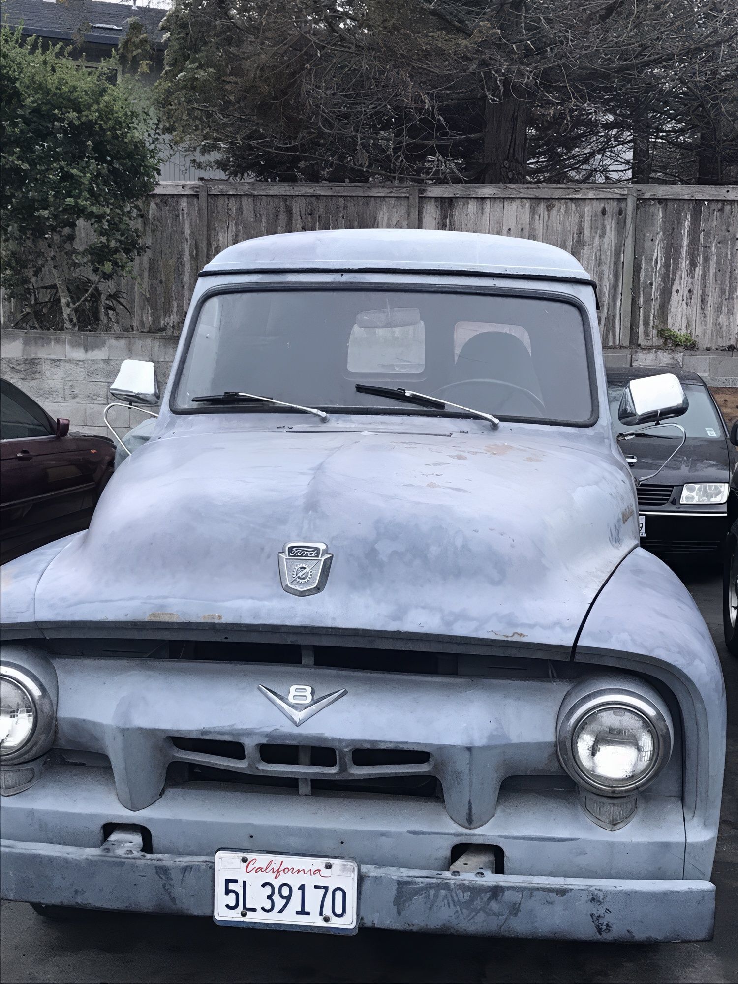 Old gray vintage pickup truck parked outdoors, covered in dust, front view with license plate visible.