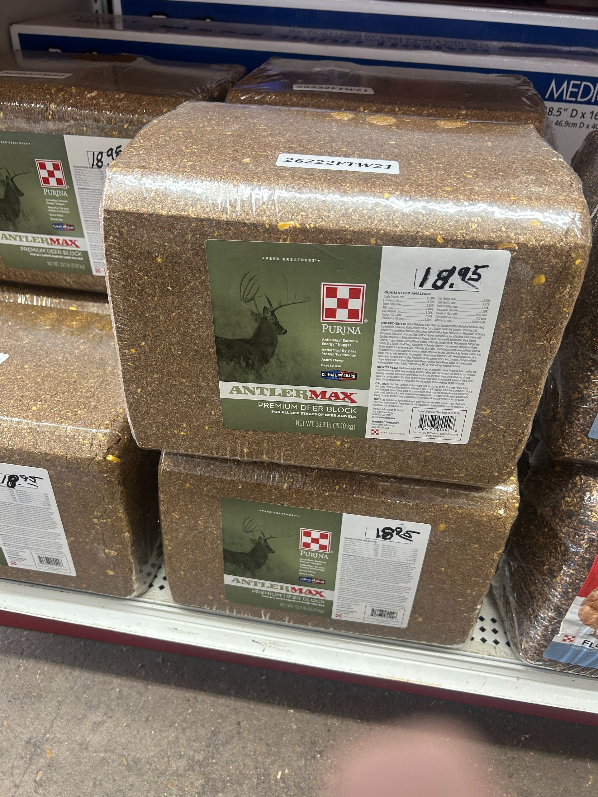 Stacks of shrink-wrapped boxes of potting soil on a store shelf, with green labels and white price tags.