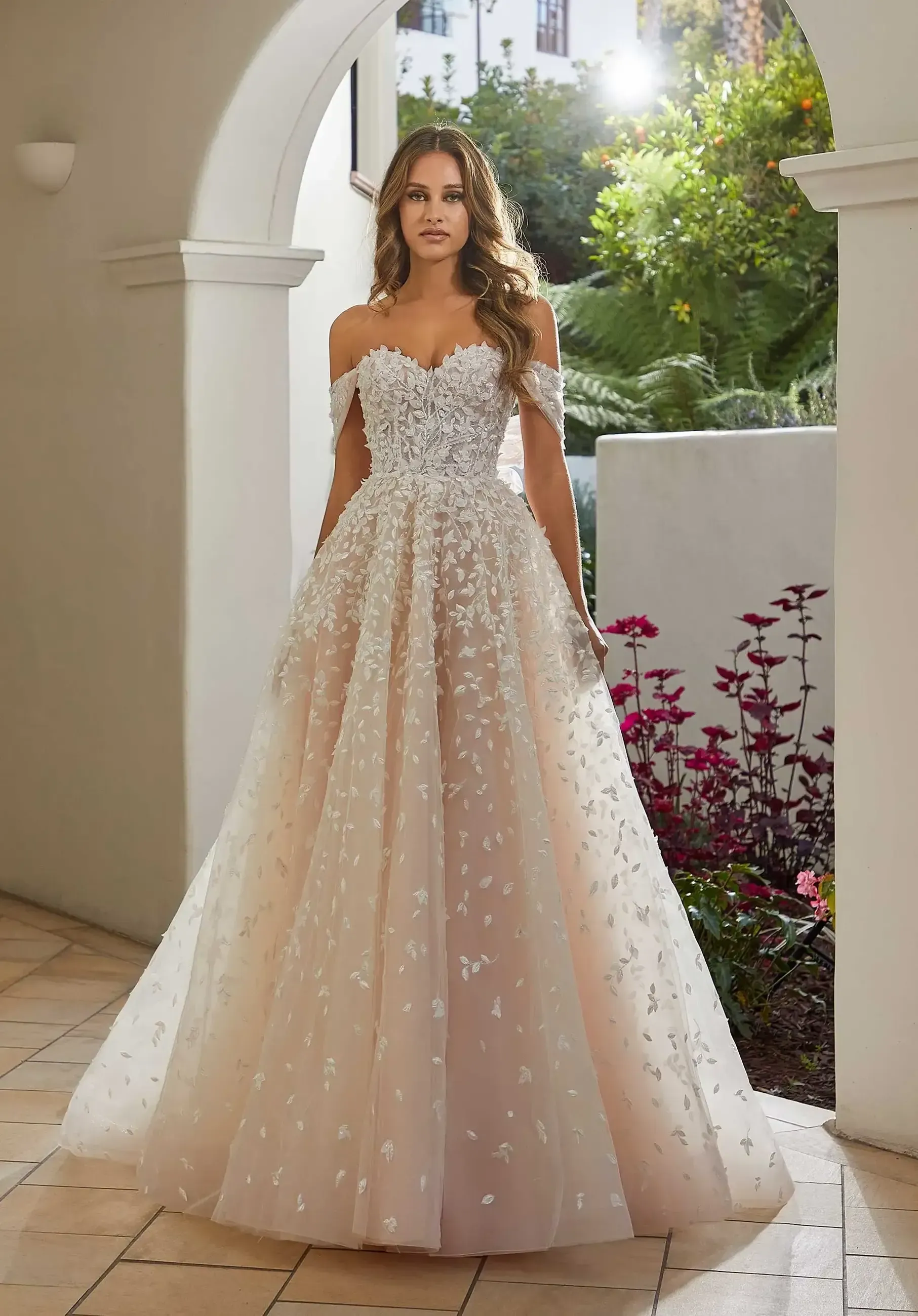 Woman in a white off-the-shoulder wedding gown poses between classical columns.