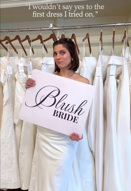 Woman in a bridal shop holding a “Blush Bride” sign while wearing an off-shoulder white dress.
