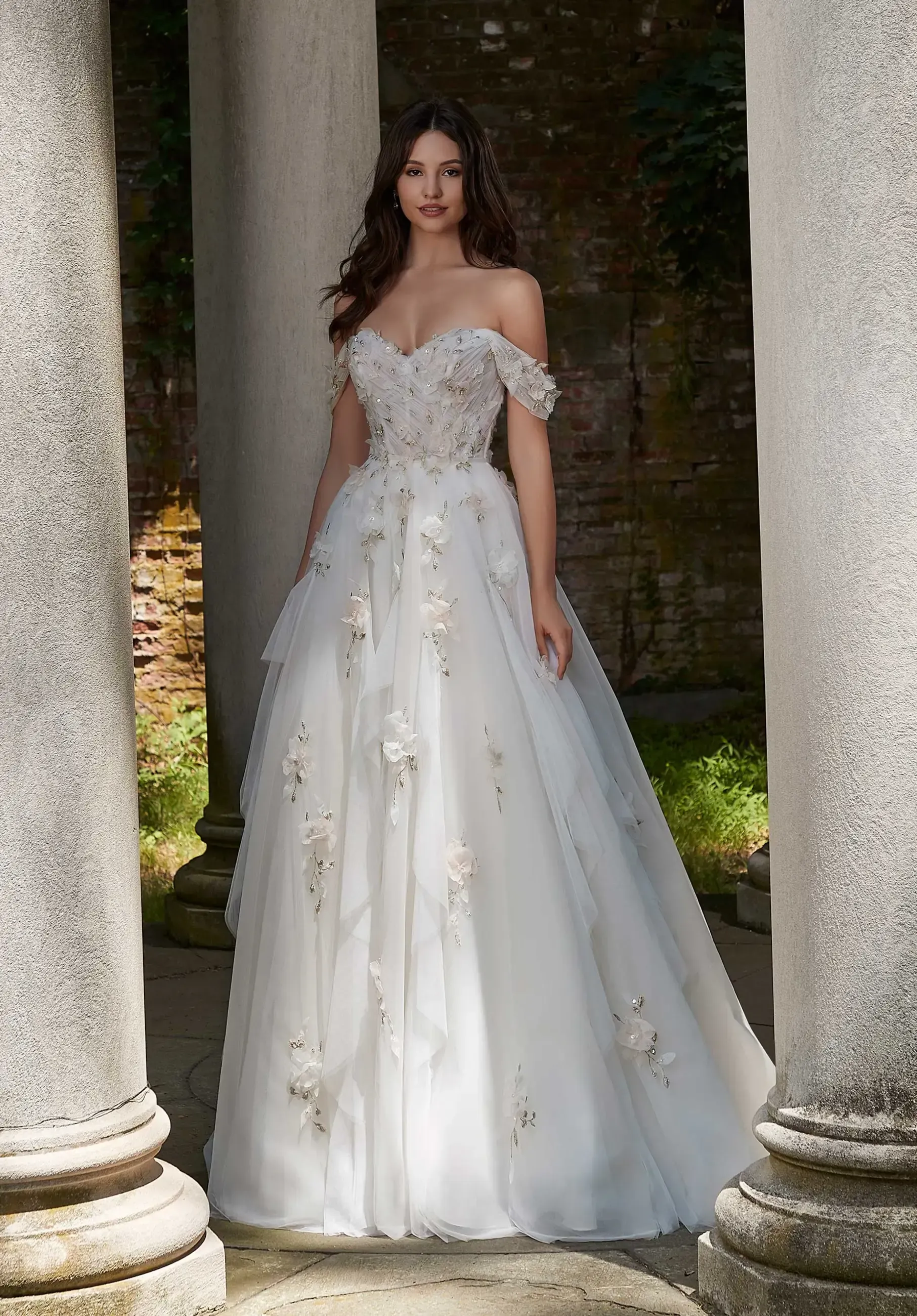 Woman in a white off-the-shoulder wedding gown poses between classical columns.