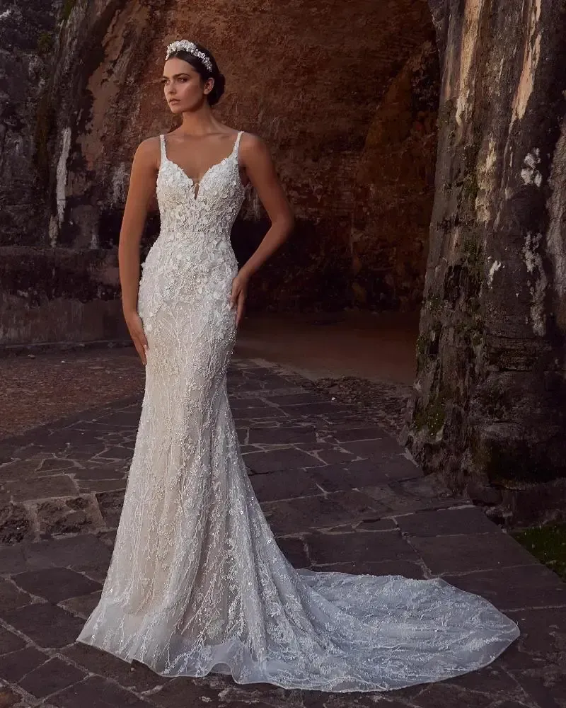 Woman in embellished wedding gown, posing outdoors, long train, thin straps, tiara.