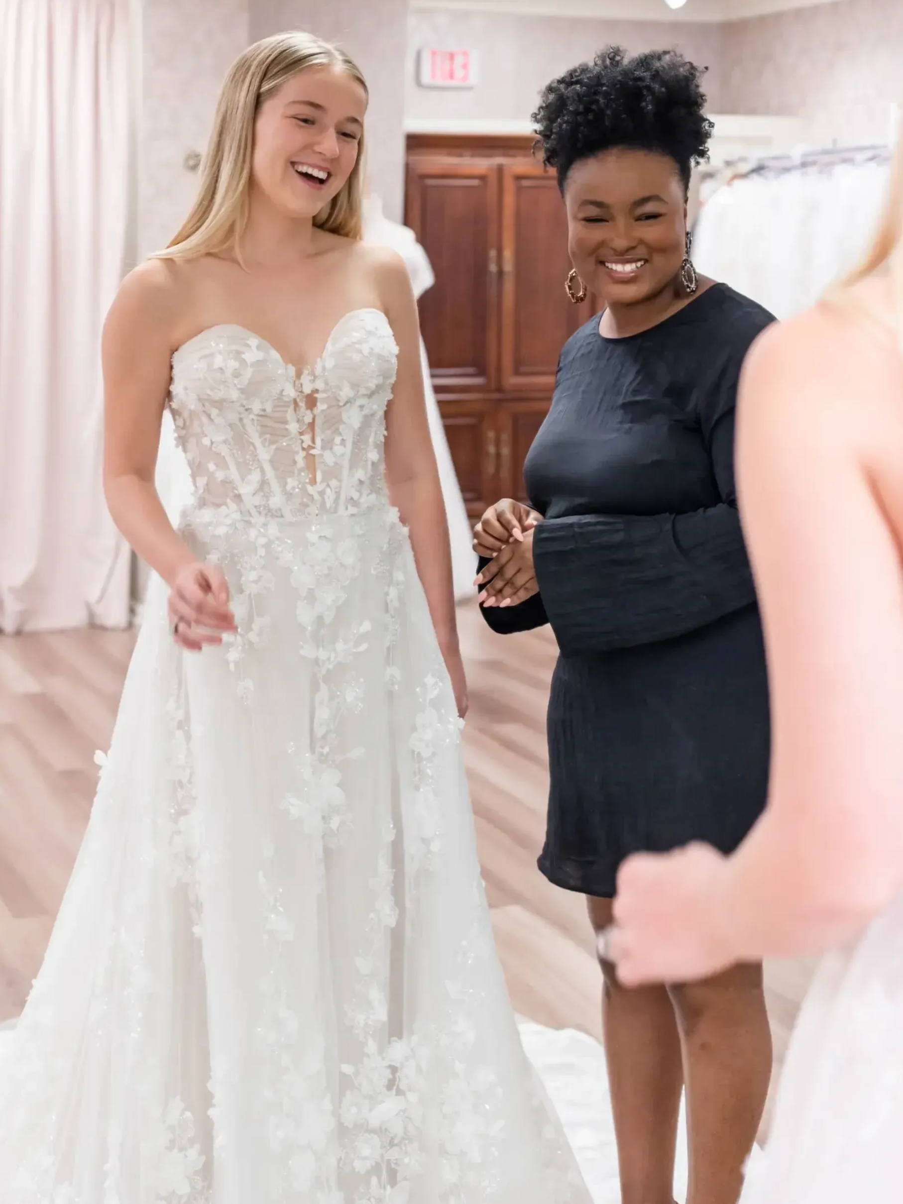 Woman in wedding dress, smiling, with consultant in bridal shop.