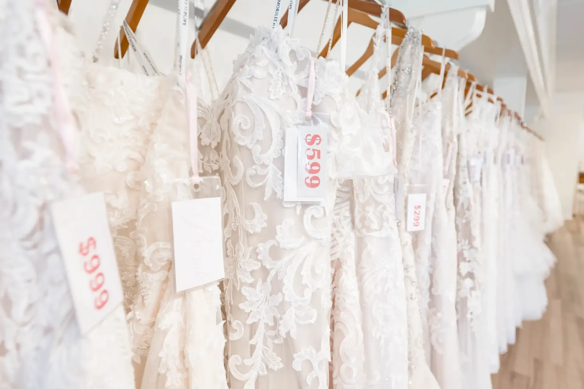 Bridal shop interior with many white wedding dresses on display, a pink sofa, and wooden floor.