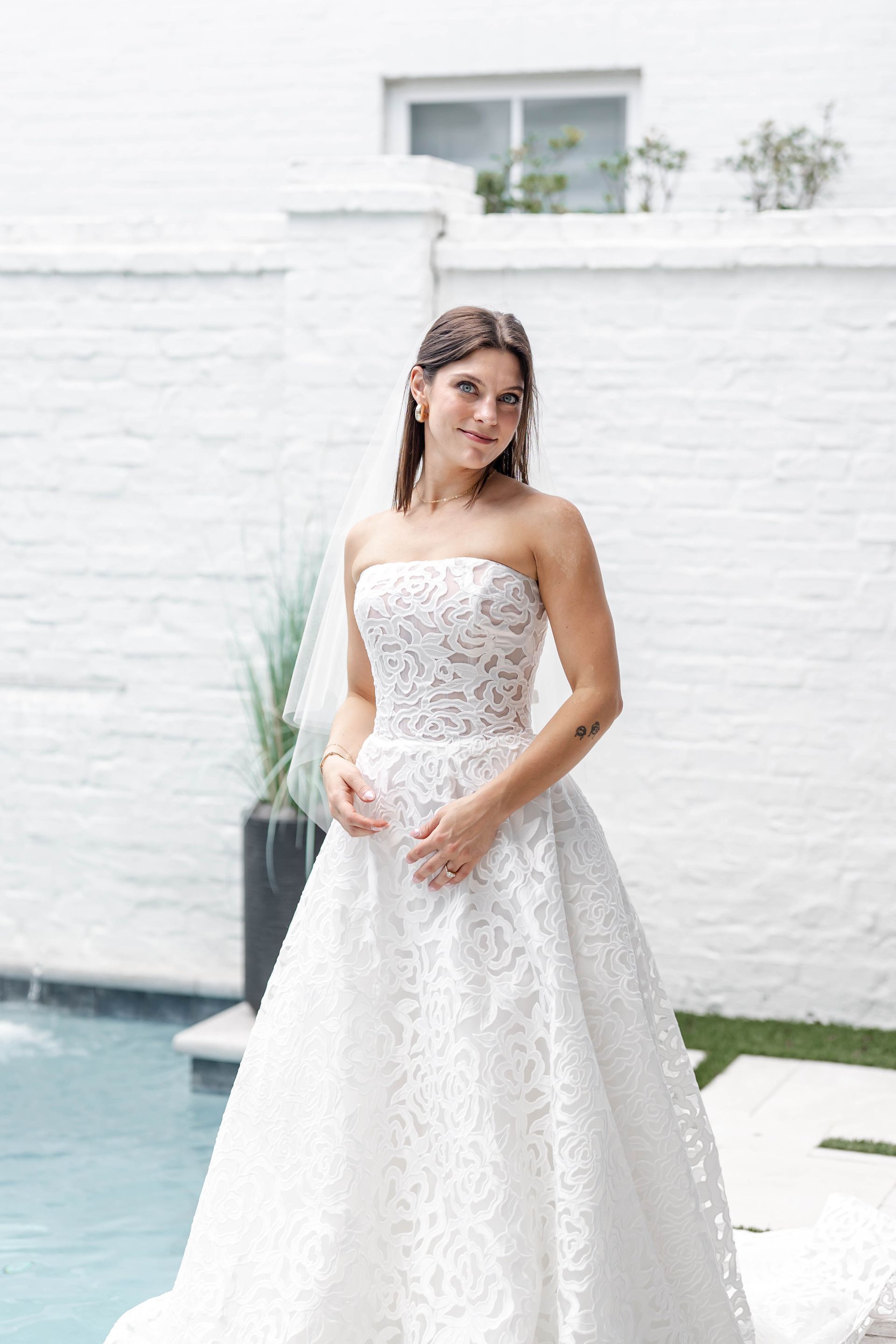 Woman in a white ball gown and tiara smiles outdoors, in front of trees.