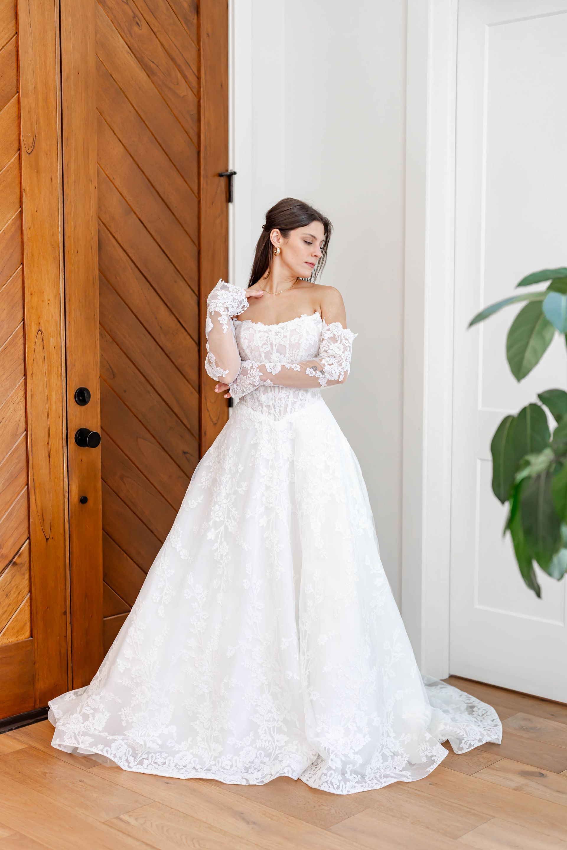 Two women in white ball gowns, tiaras, and gloves hold bouquets. They stand in front of a black backdrop.
