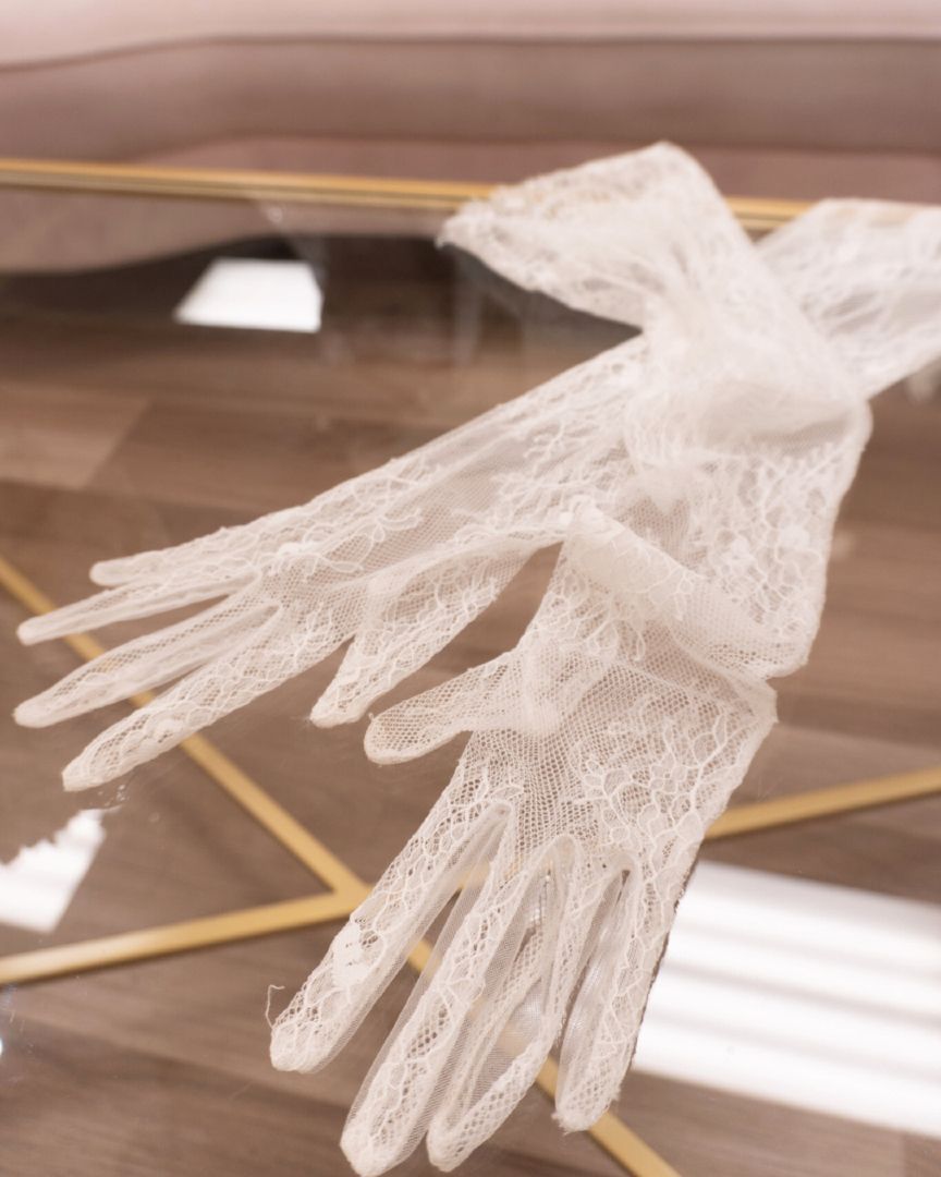 White lace gloves on a glass surface with a gold frame, angled perspective.