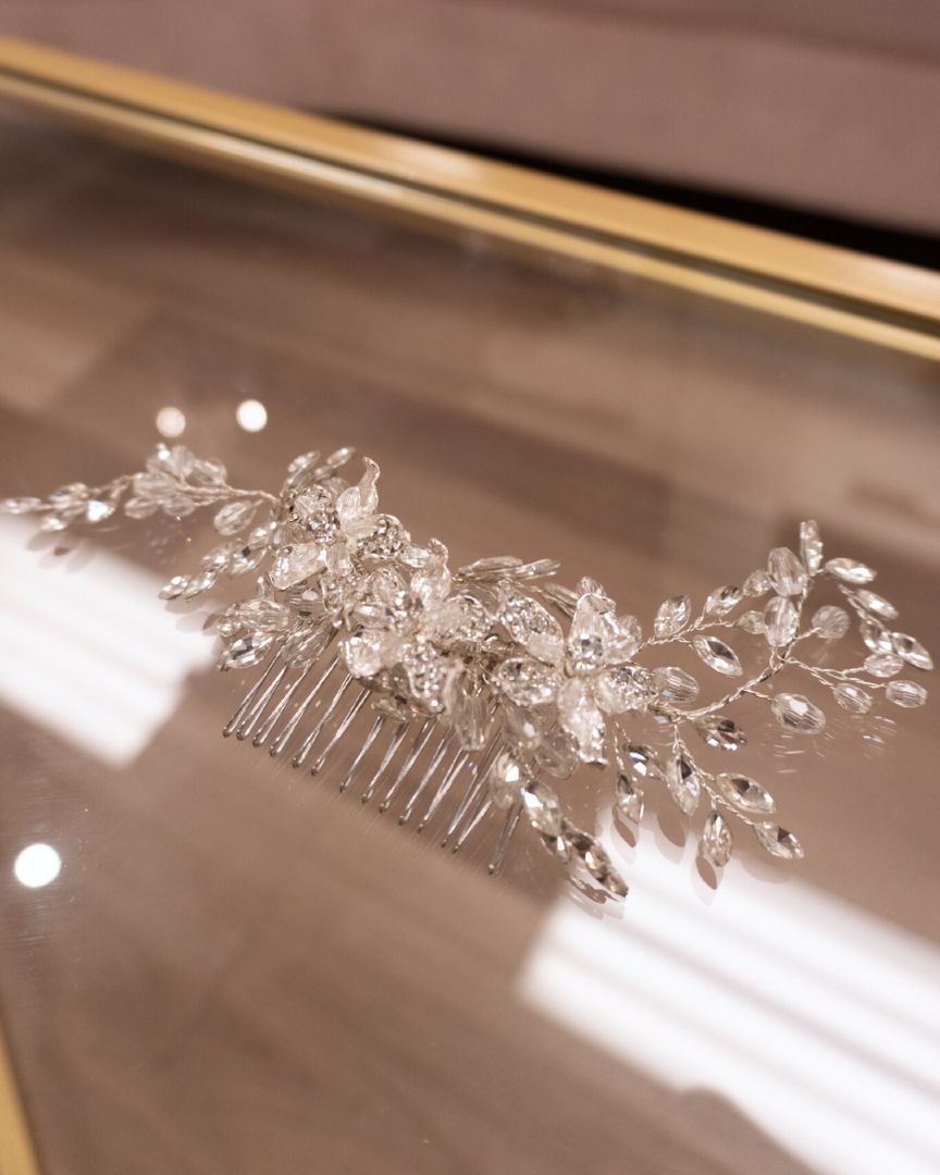 Silver bridal hair comb with crystal accents on a reflective surface.
