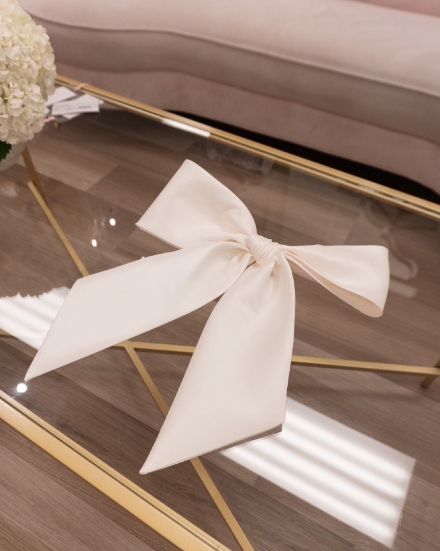 Cream-colored bow on a clear, gold-framed glass table, with a pink sofa in the background.