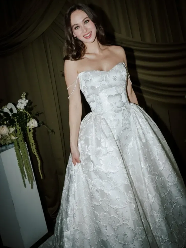 Woman in strapless white gown, smiling, indoors.
