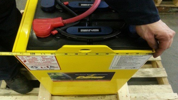 A person is measuring a yellow battery with a tape measure
