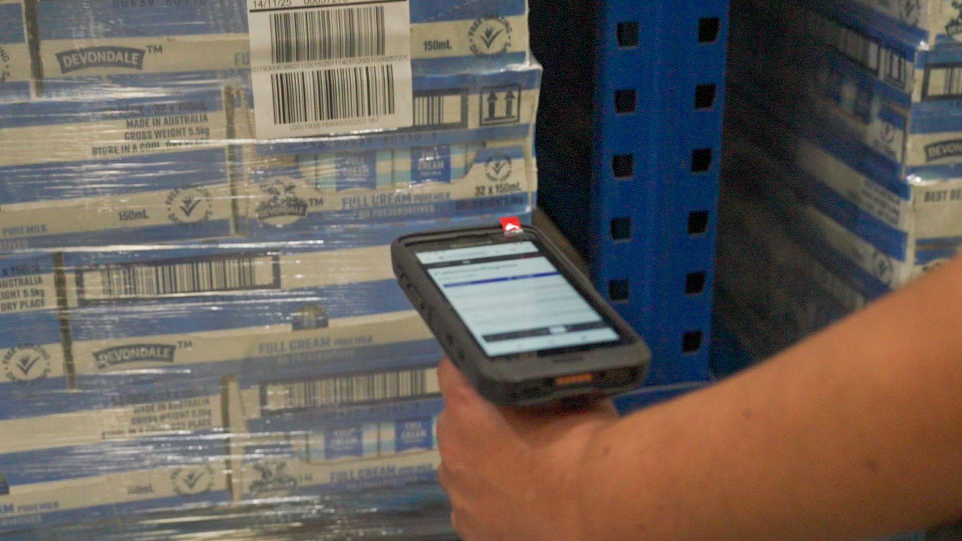 A person in a warehouse scans a barcode on a pallet of products using a handheld mobile device.