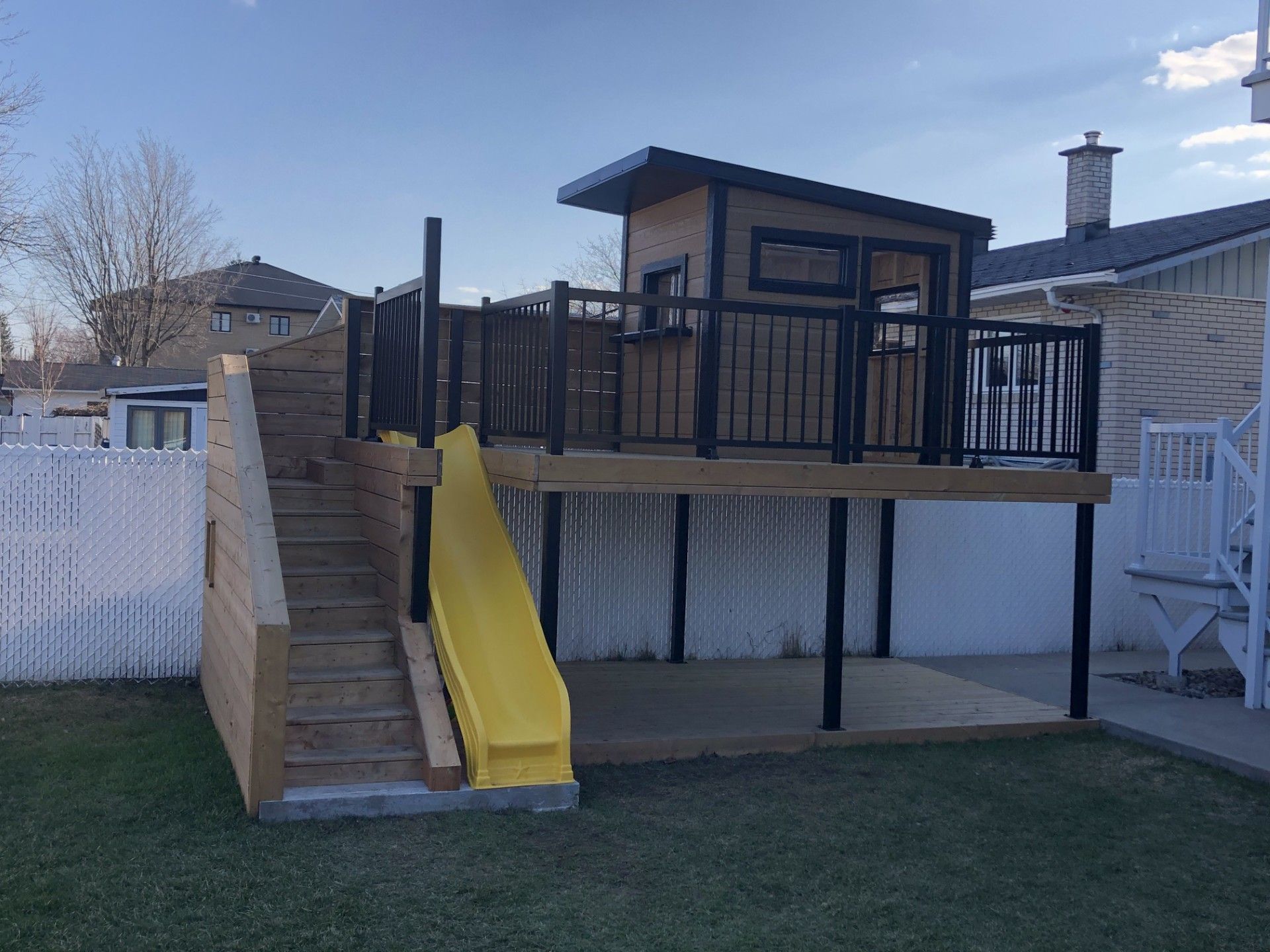 Une cabane dans les arbres avec un toboggan et des escaliers dans l'arrière-cour d'une maison.