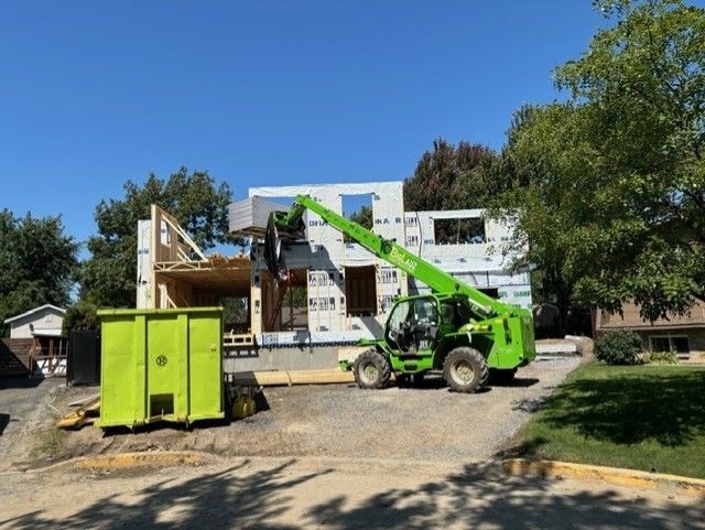Un chariot élévateur vert est garé devant une maison en construction.