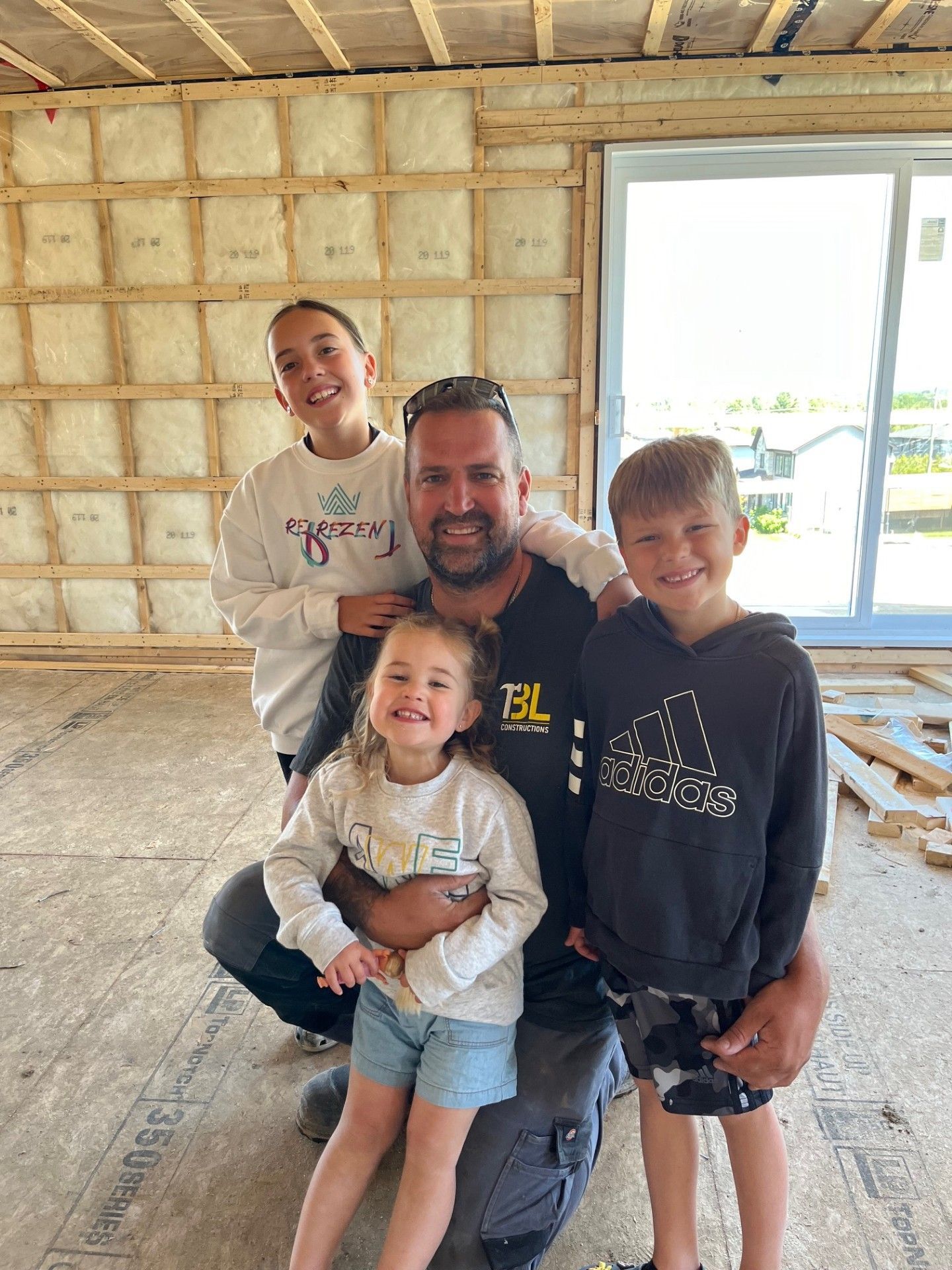 Un homme et trois enfants posent pour une photo dans une pièce en travaux.