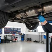 Mechanic inspecting a car’s exhaust system on a lift in a bright auto repair shop | PC Auto Repair