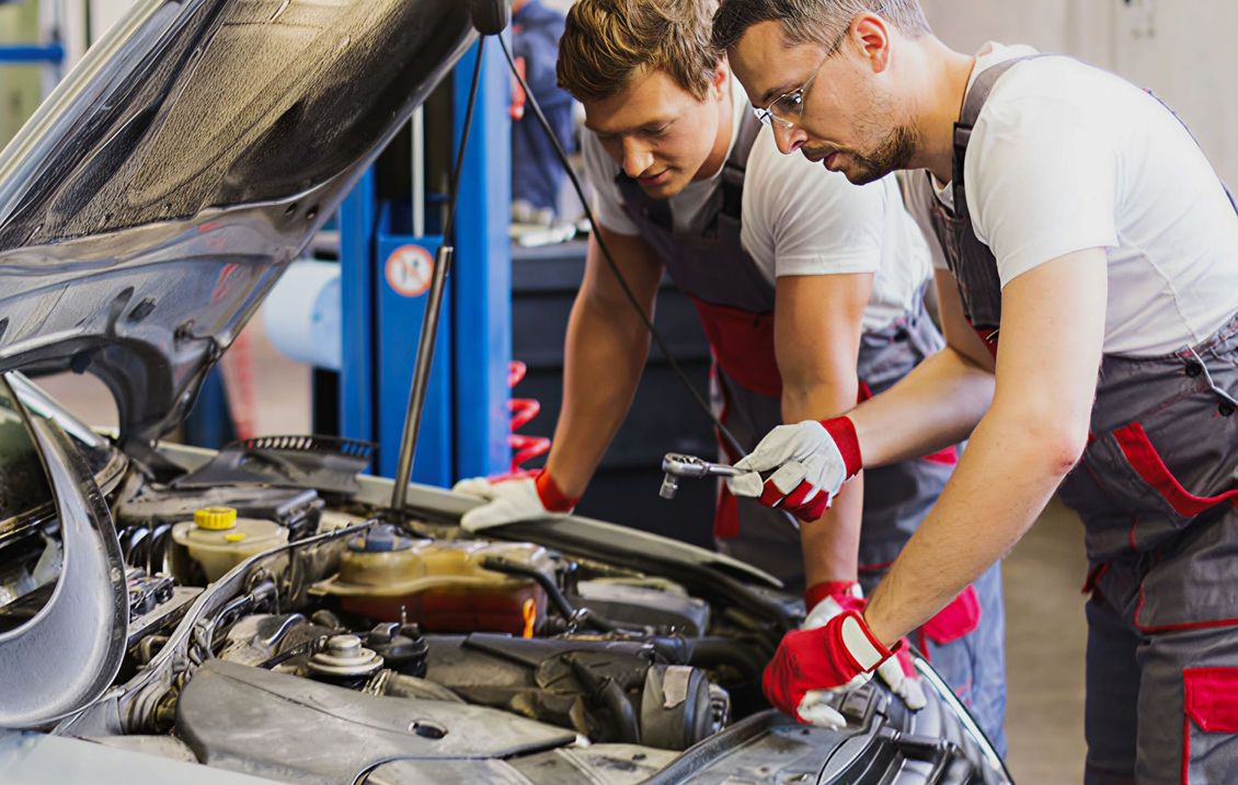 Two mechanics in red gloves inspect an open car engine in a garage. | PC Auto Repair