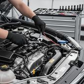 Mechanic using a wrench on a car engine in a repair shop, with gloved hands and open hood. | PC Auto Repair