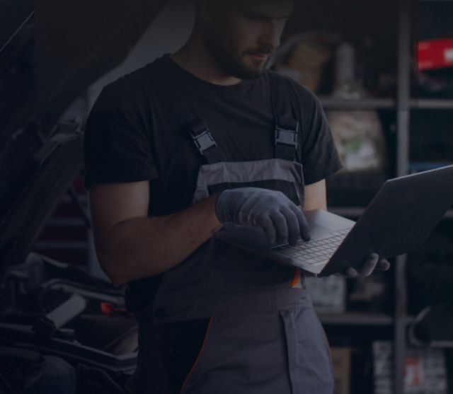 Mechanic in gray overalls using a laptop in a dim garage | PC Auto Repair