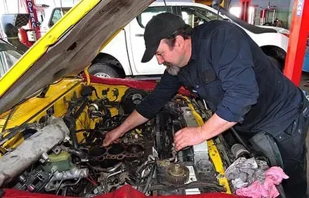 A Man is Working on the Engine of a Yellow Car — Reliable Bus and Truck Repairs In Caloundra West, QLD
