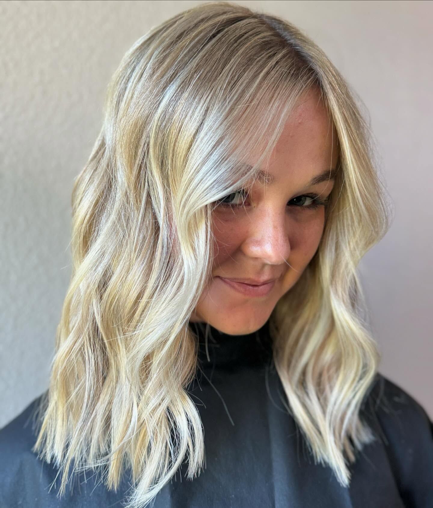 A person with shoulder-length, wavy blonde hair with highlights, smiling gently at the camera.