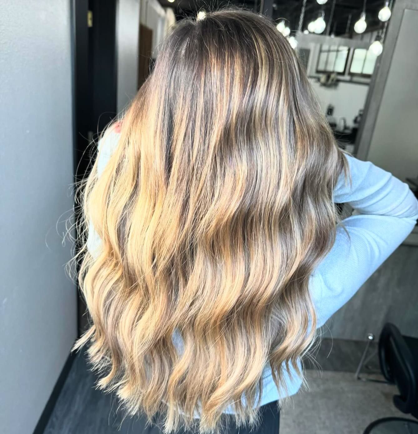 Back view of long, wavy hair with a blended balayage of dark brown roots transitioning into light blonde lengths.