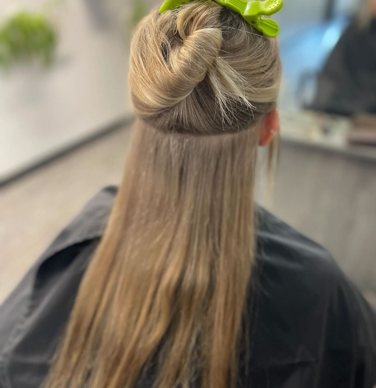 Light brown hair styled in a half-up bun with a neon green clip, seen from behind in a salon setting.