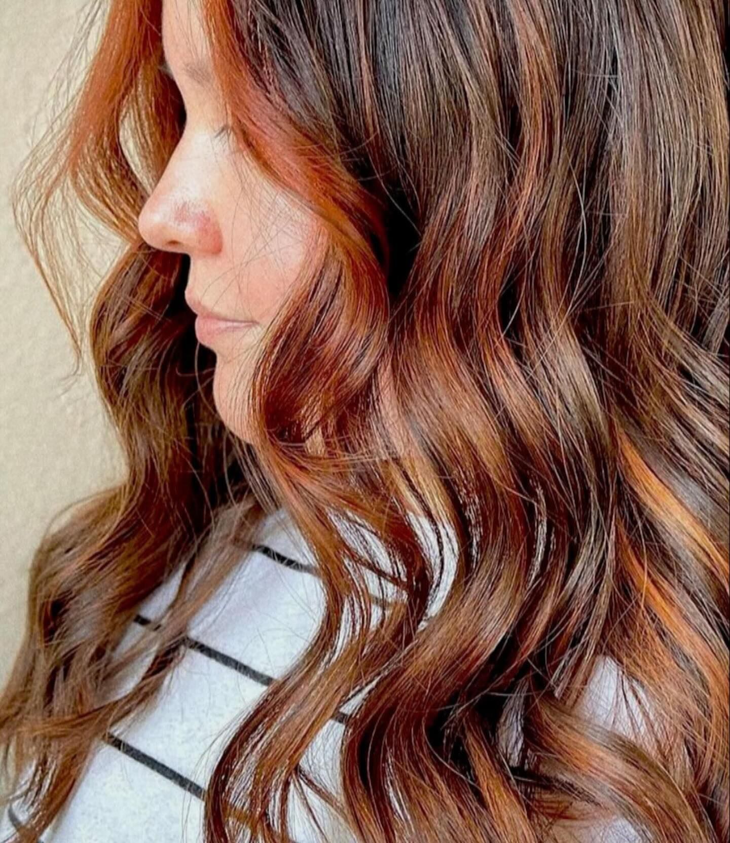 A side profile view of wavy, medium-brown hair with vibrant auburn and copper highlights.