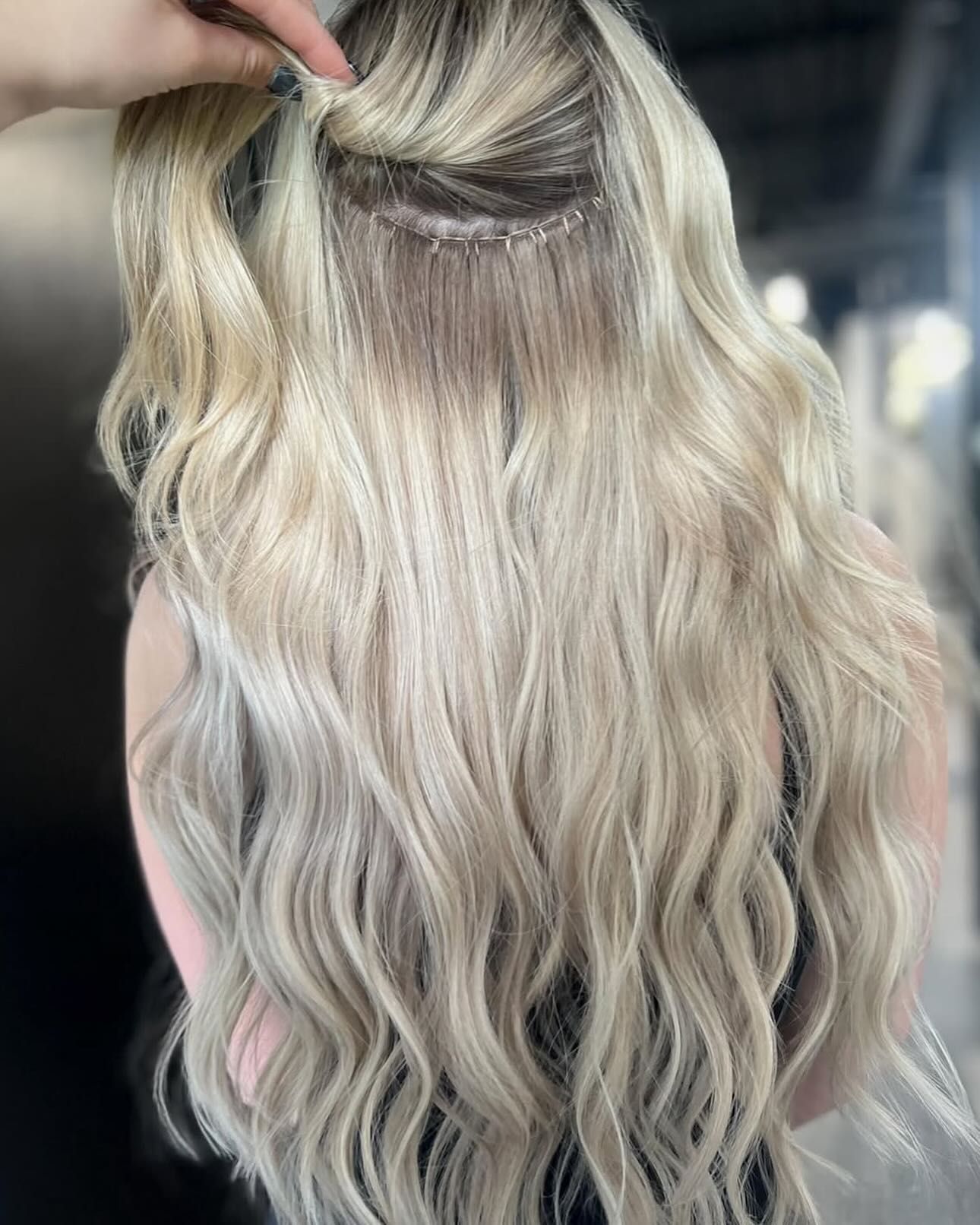 A close-up of a person's light blonde hair showing a horizontal weft extension secured with visible thread.