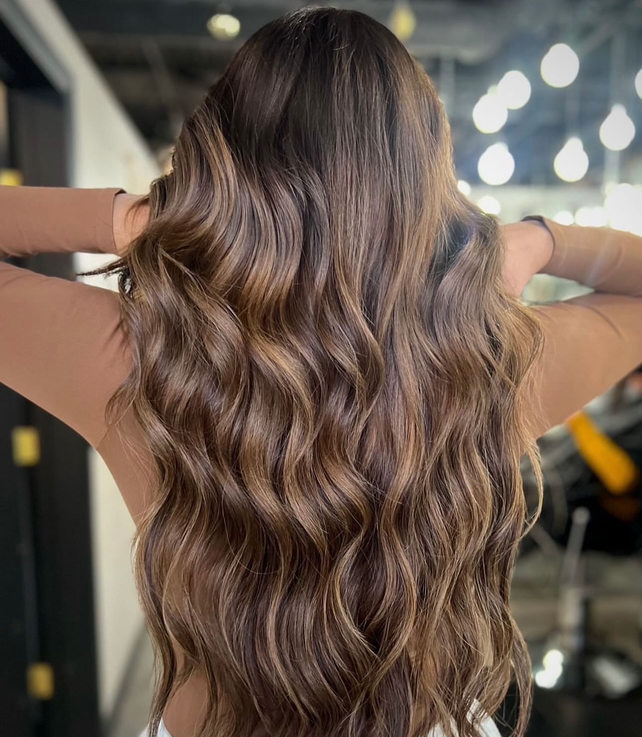 Back view of long, wavy brunette hair with light brown highlights, styled in loose curls.