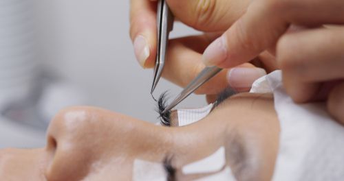 A technician uses tweezers to carefully apply individual eyelash extensions to a client’s eyelid.