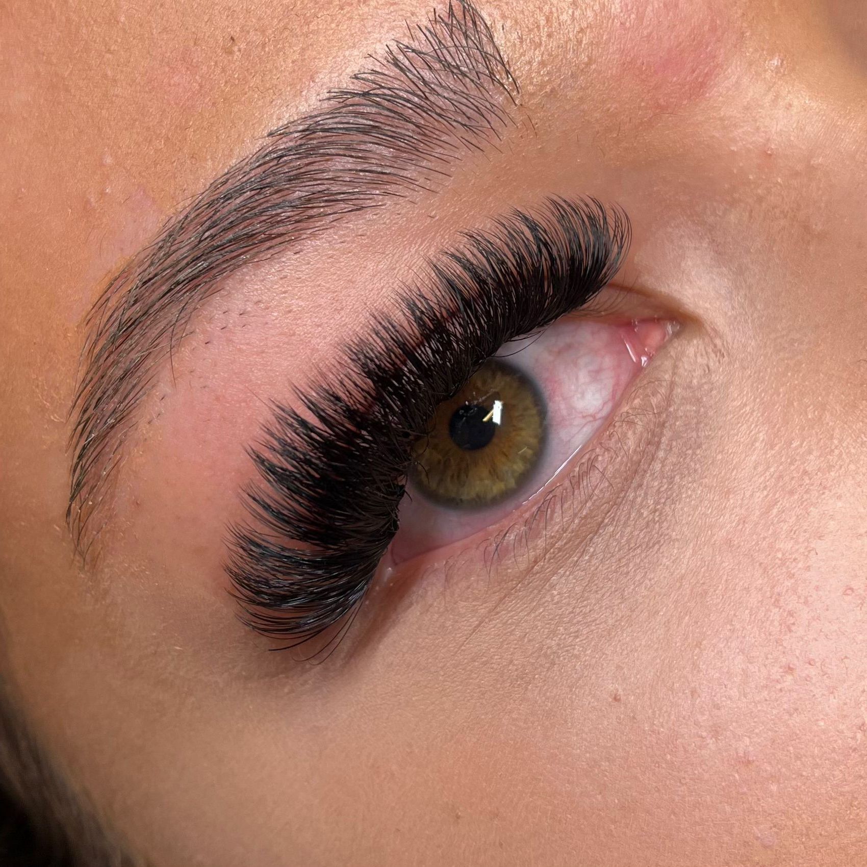 Close-up van een oog met dikke, donkere wimperextensions en netjes verzorgde, microbladed wenkbrauwen.