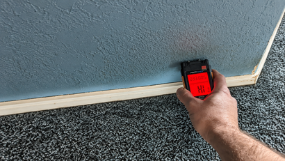 Hand holding a red digital device against a blue wall and carpeted floor.