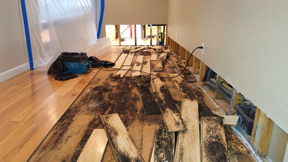 Flood-damaged hallway with water-soaked floorboards, mud, and debris along the walls.