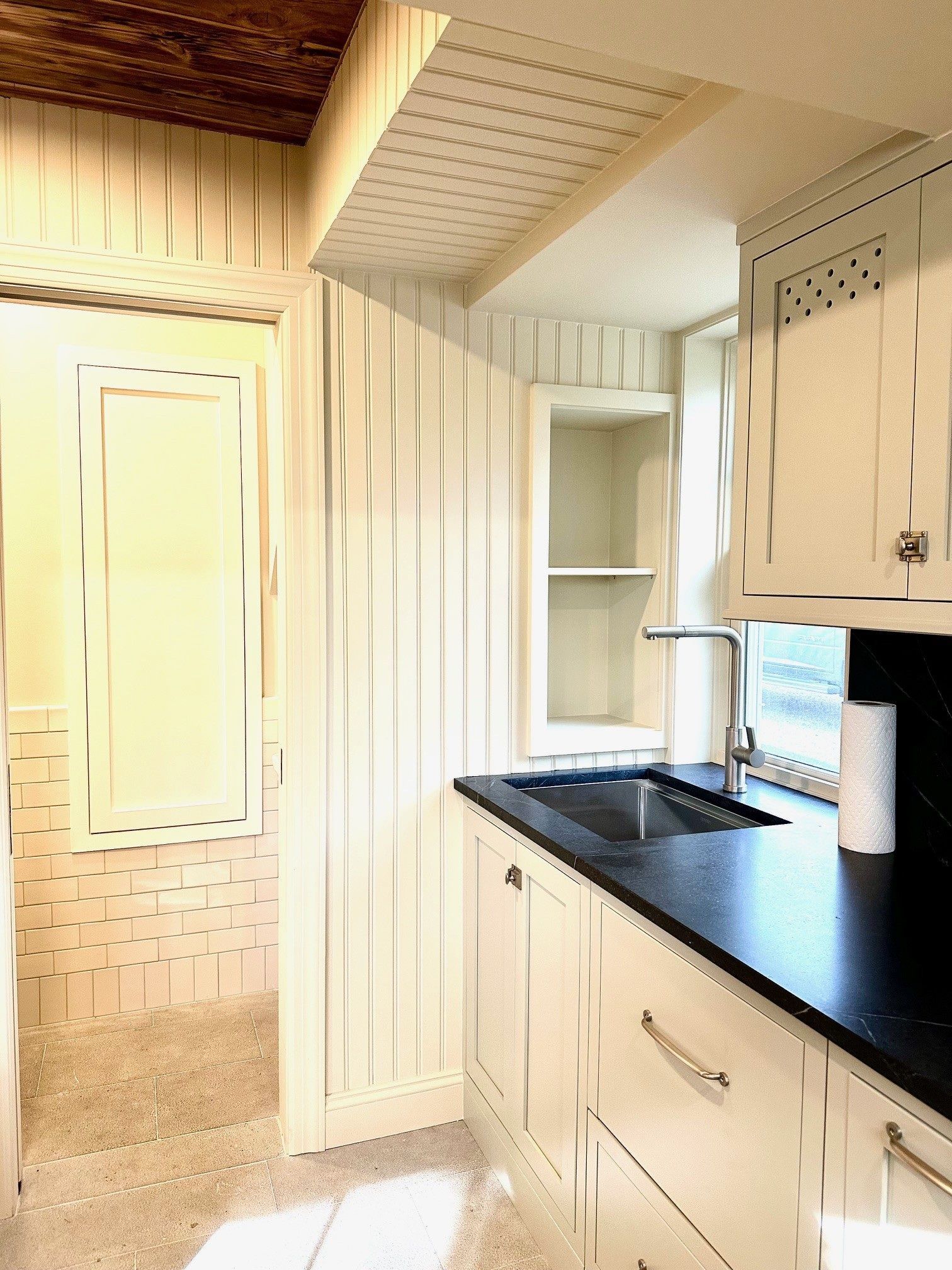 Small kitchen with cream cabinets, black countertop, sink, and narrow hallway opening to the left.