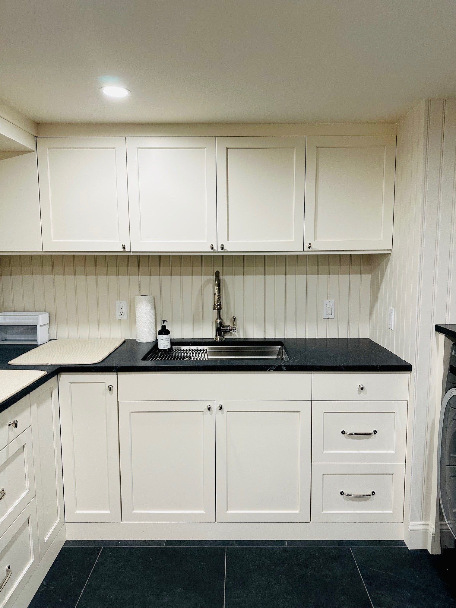 White kitchen with black countertops, white cabinets, sink, and a microwave on the left.