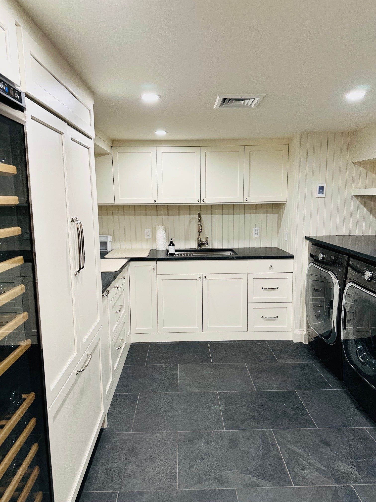 Modern white kitchen with black countertops, tiled floor, and built-in oven and cabinets