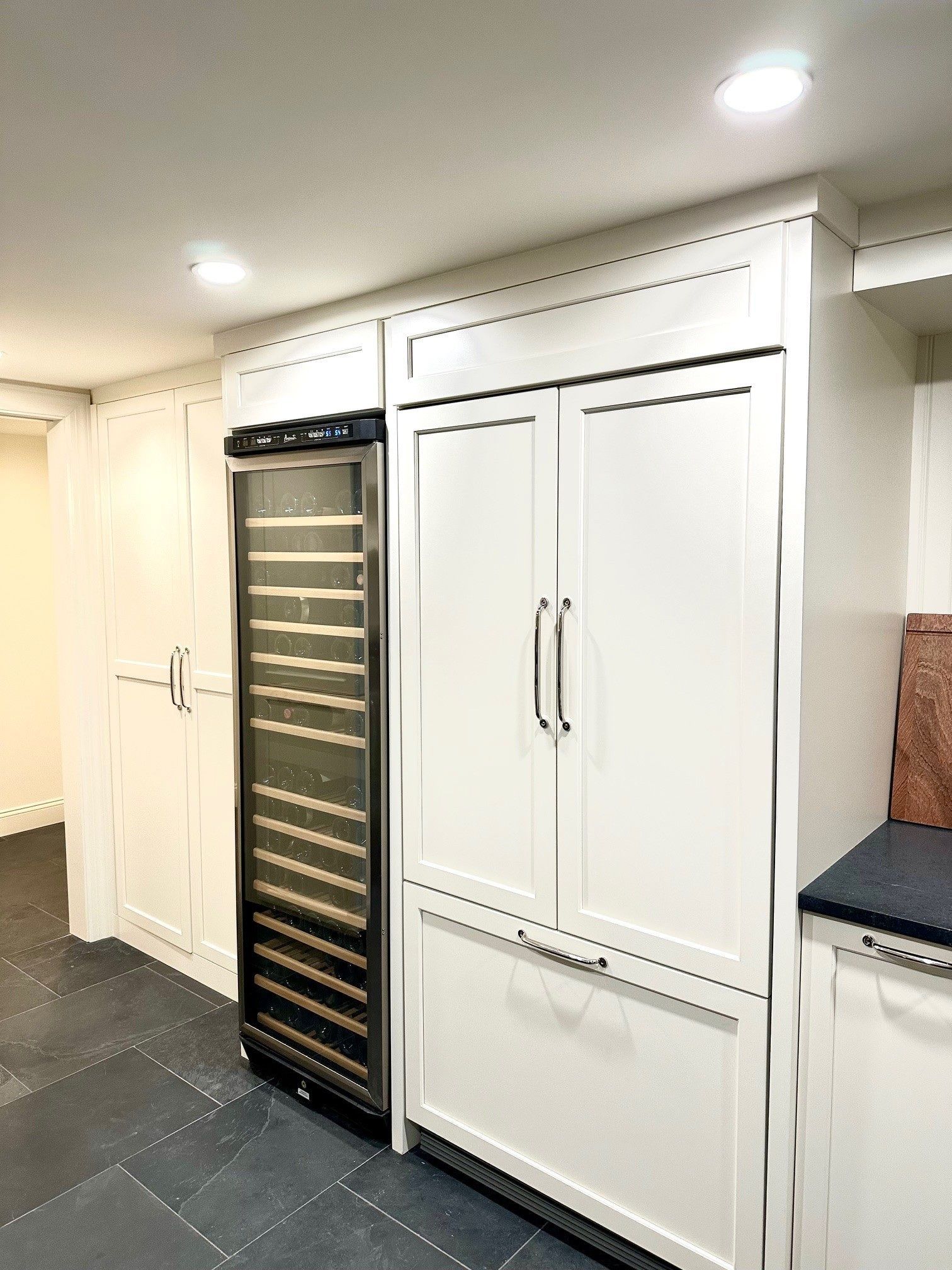 Built-in white storage cabinets beside a black wine fridge in a bright kitchen area