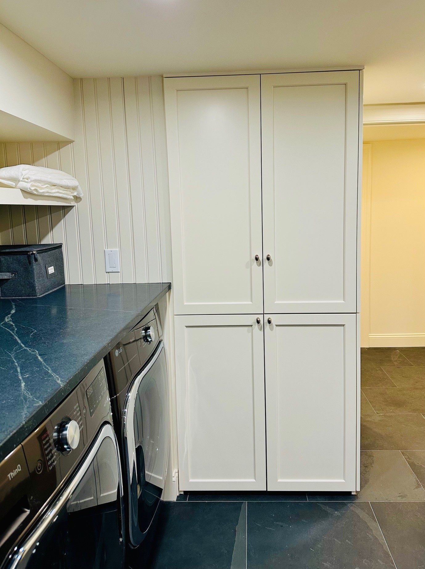 Kitchen with white built-in pantry cabinets beside a dark countertop and stainless-steel stove.