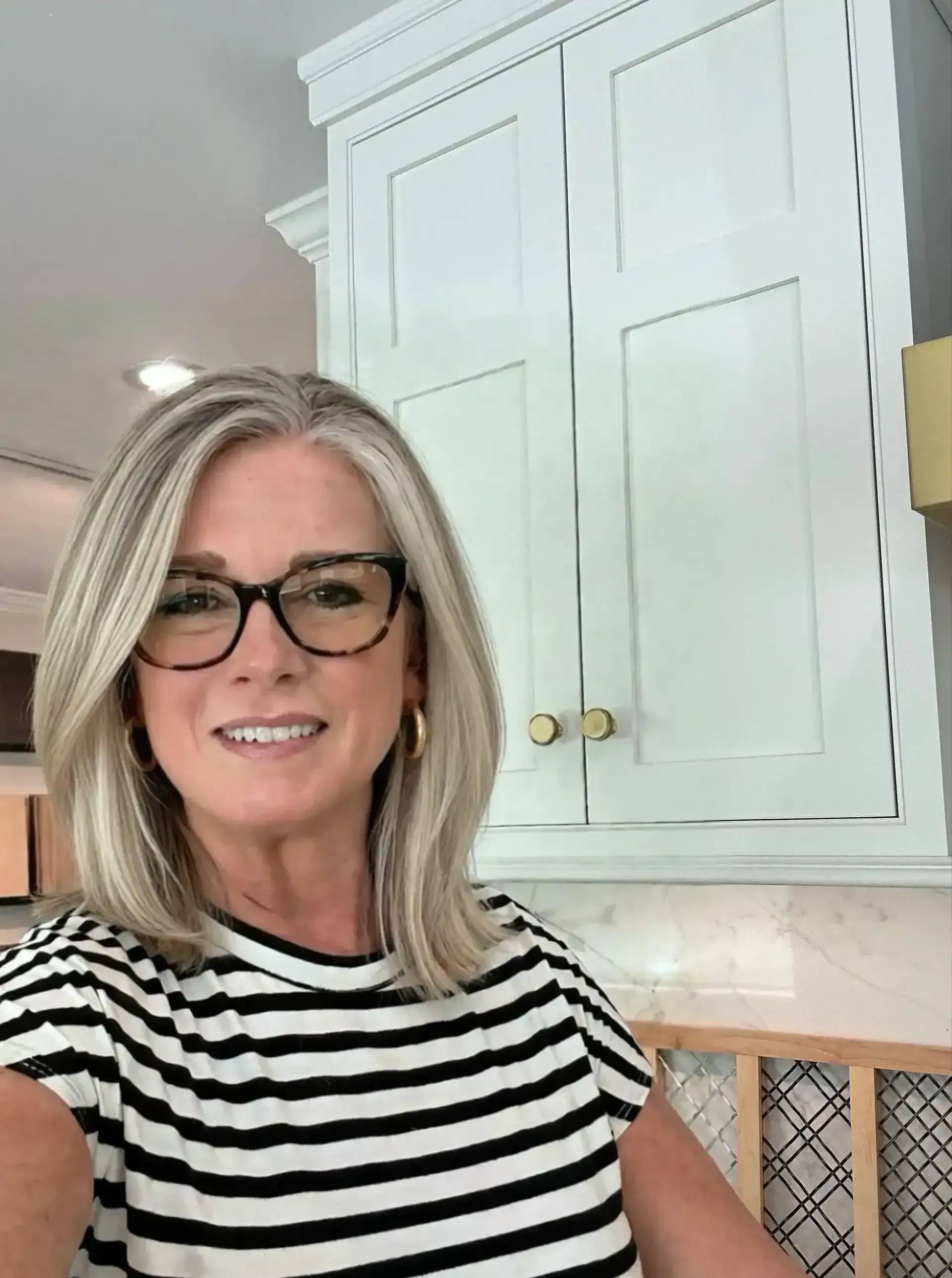Smiling woman in glasses and striped shirt standing in a bright kitchen