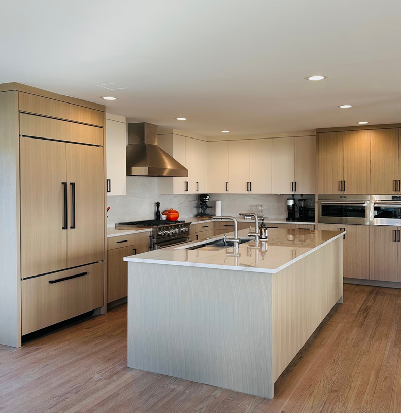 Modern kitchen with light wood cabinets, a large island, stainless appliances, and wood flooring.