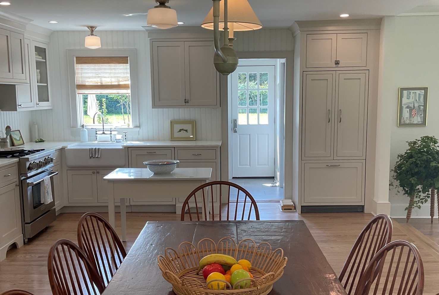 Bright kitchen with dining table, fruit basket, white cabinets, and a door to a sunlit patio.