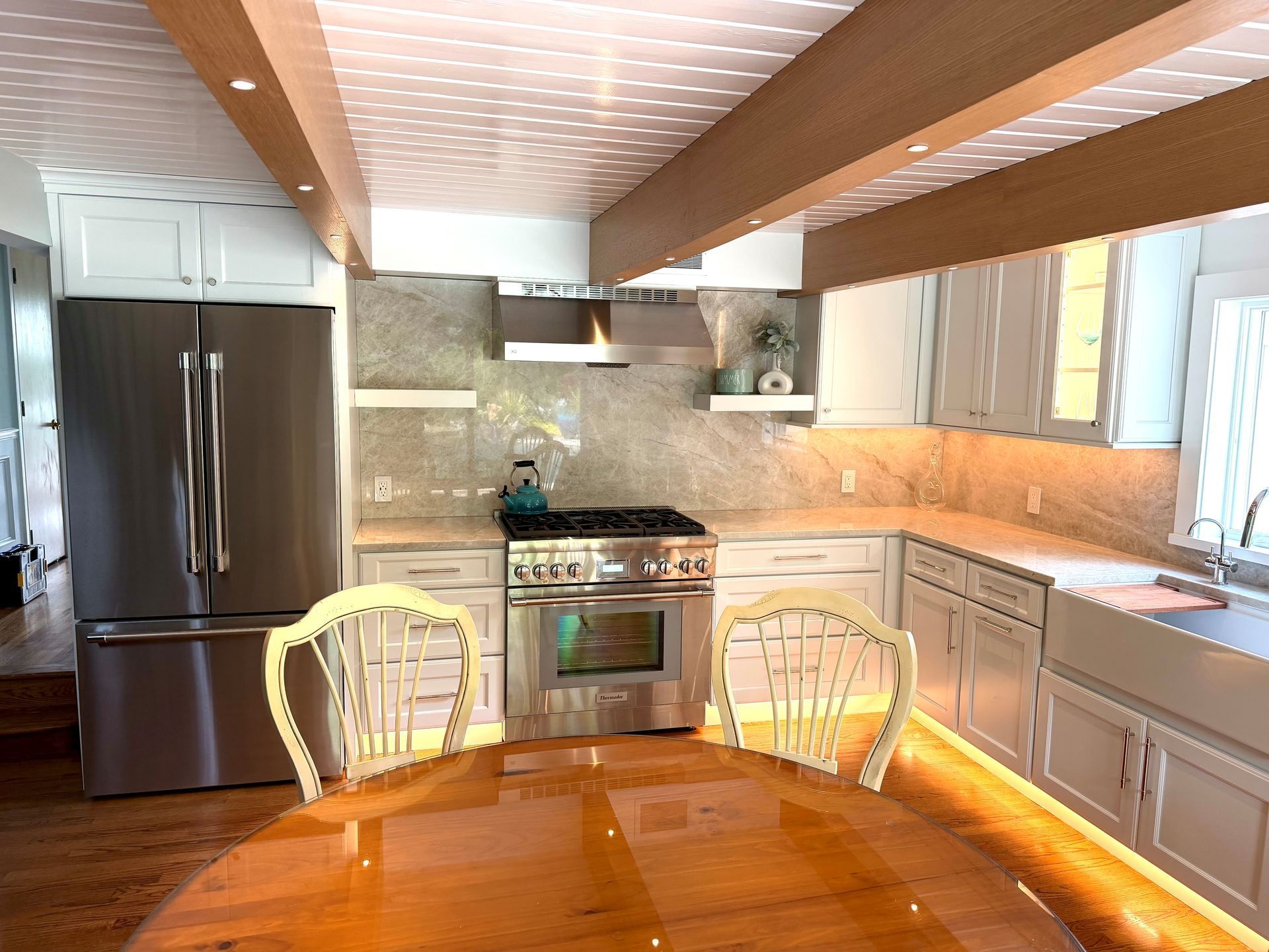 Bright kitchen with stainless steel appliances, white cabinets, and a wooden table in the foreground